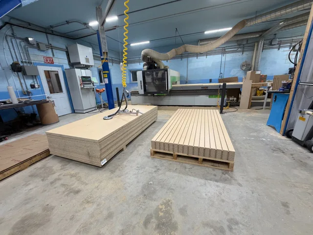 CNC-routed slatwall panels and sheet stock beside a Biesse router at Cedar Hedge Millworks