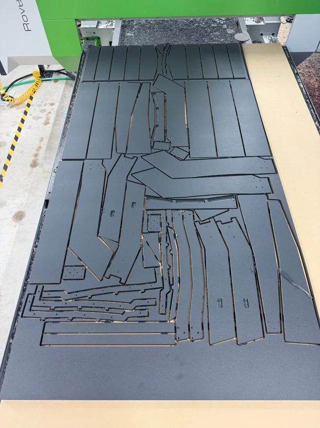 Black plastic furniture components tightly nested and cut on a Biesse CNC routing table